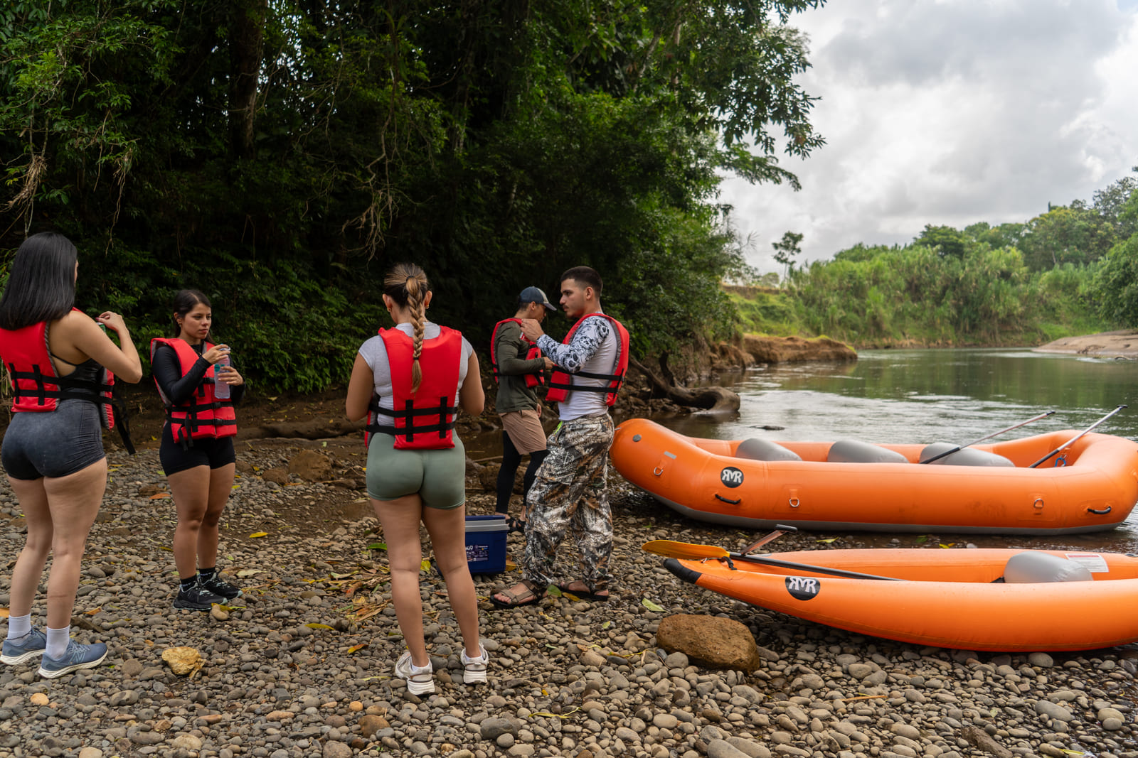 Guía dando briefing al grupo en la orilla rocosa con rafts y kayaks varados al final del recorrido