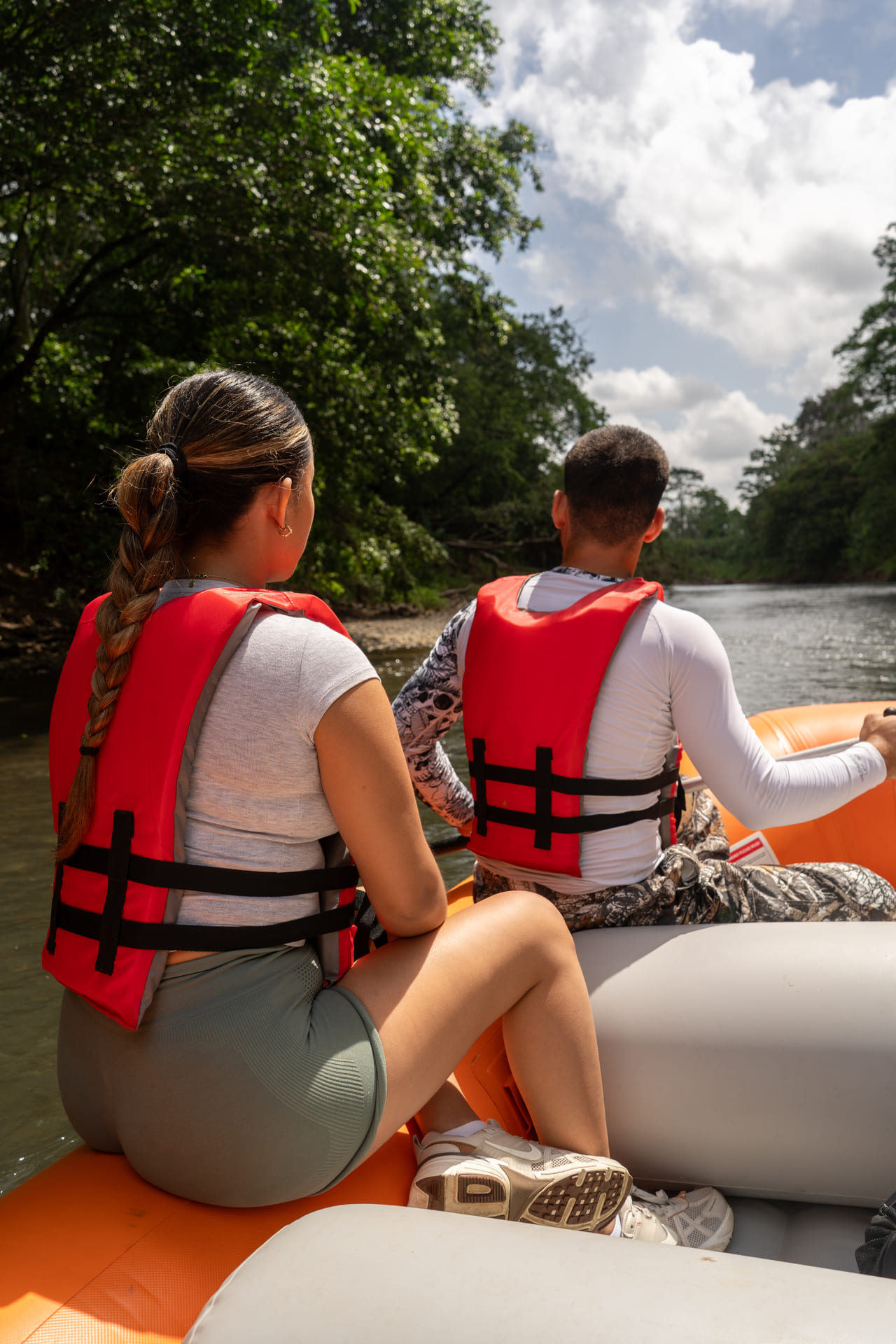 Pareja sentada en la proa de la balsa con el cielo abierto sobre el río