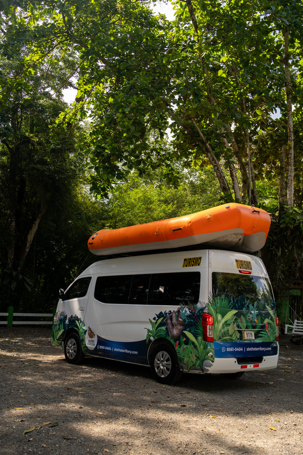 Microbús turístico branded con raft inflable naranja sobre el techo, llegando al embarcadero