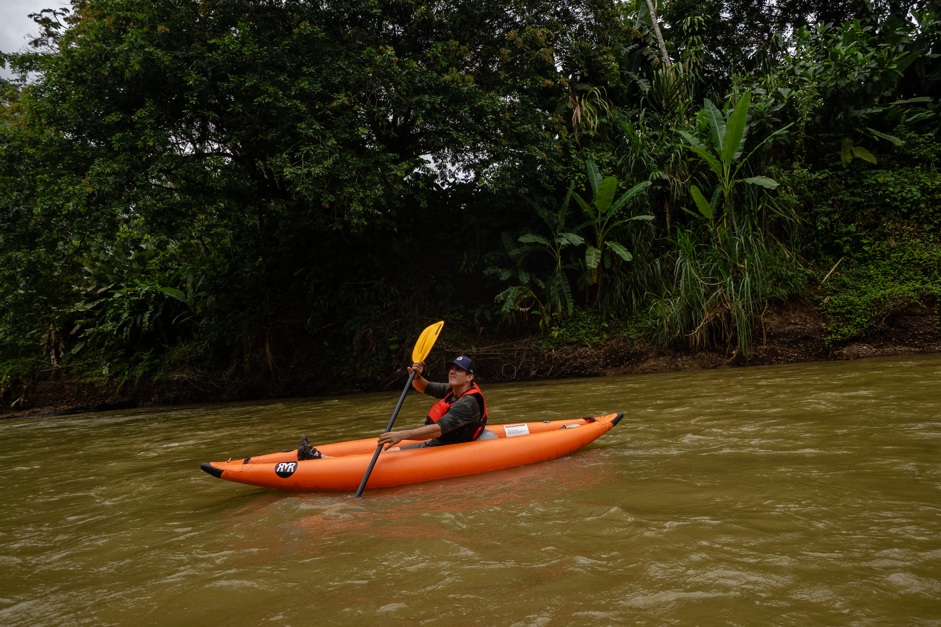 Naturalist guide paddling an orange inflatable kayak on a river in La Fortuna